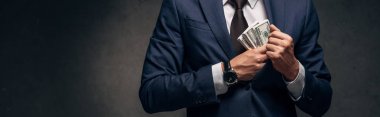 panoramic shot of businessman in suit putting cash in pocket on grey  clipart