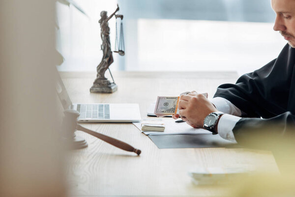 selective focus of judge holding money near wooden gavel on table 
