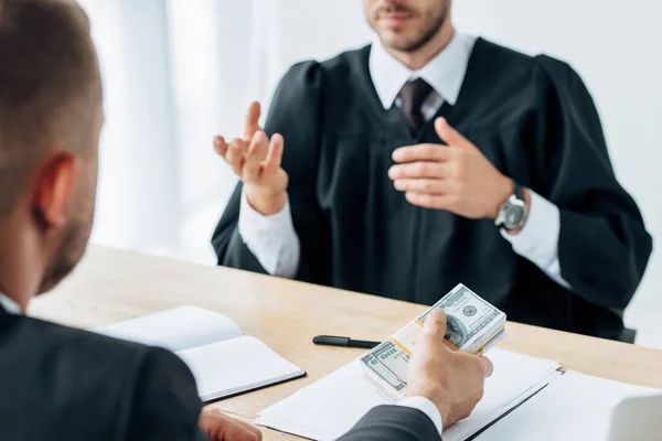 selective focus of man giving money to judge sitting and gesturing near table