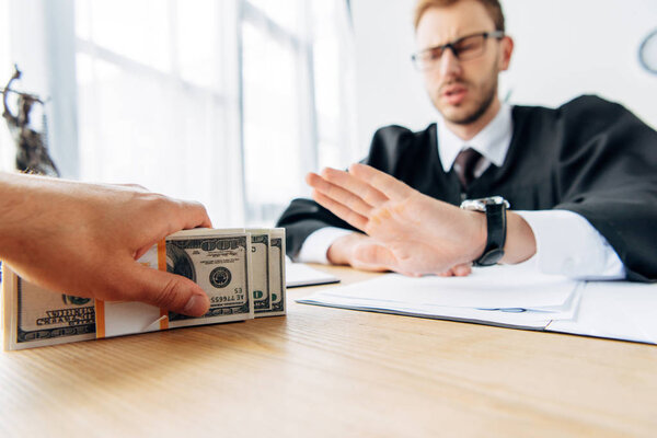 selective focus of man holding cash near judge gesturing in office 