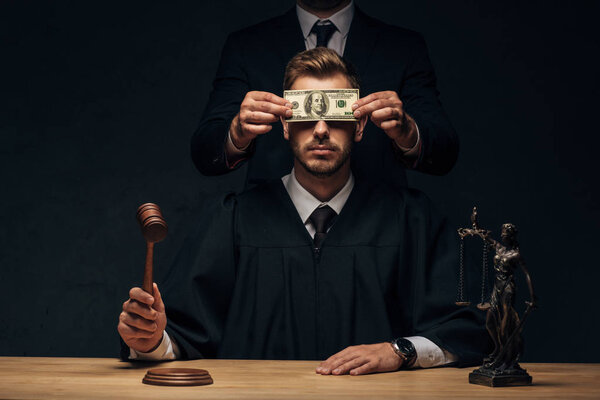 cropped view of man standing and covering face of judge with bribe on black 