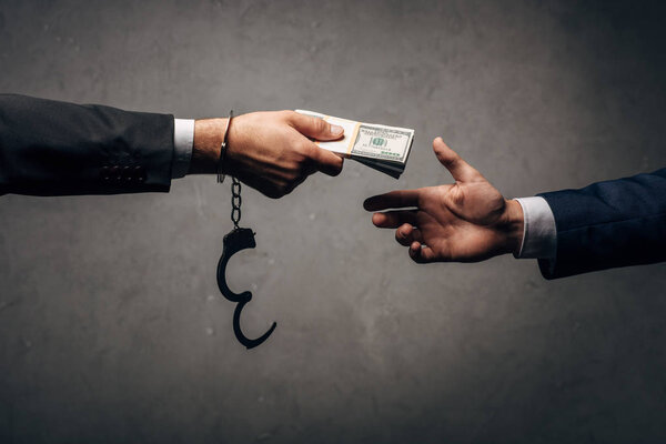 cropped view businessman in handcuffs giving bribe to business partner on grey 