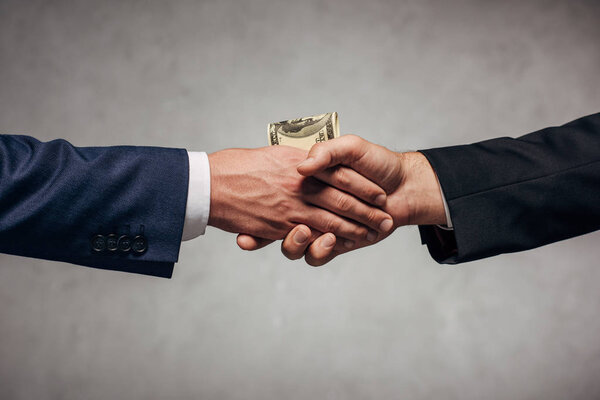 cropped view man shaking hands with business partner while giving money on grey 