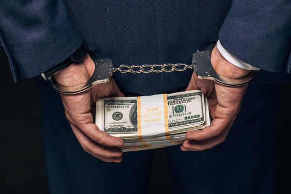 close up of handcuffed man in formal wear holding bribe on grey 