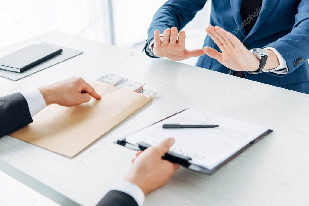 selective focus of man holding clipboard and pointing with finger at contract with pen near business partner gesturing in office 