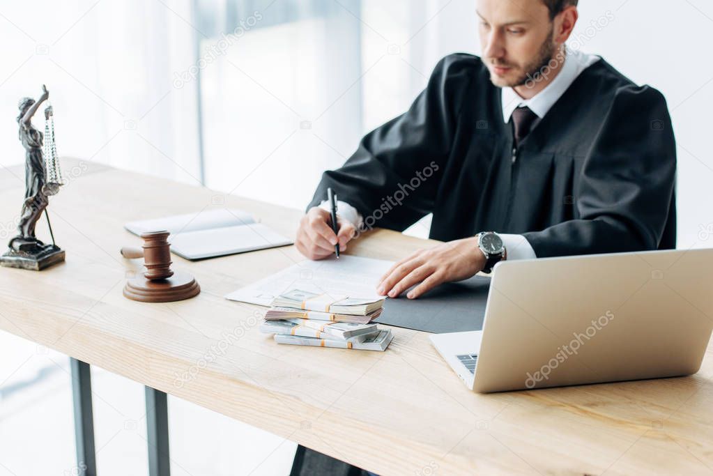 selective focus of laptop near gavel and money near judge and money on table  