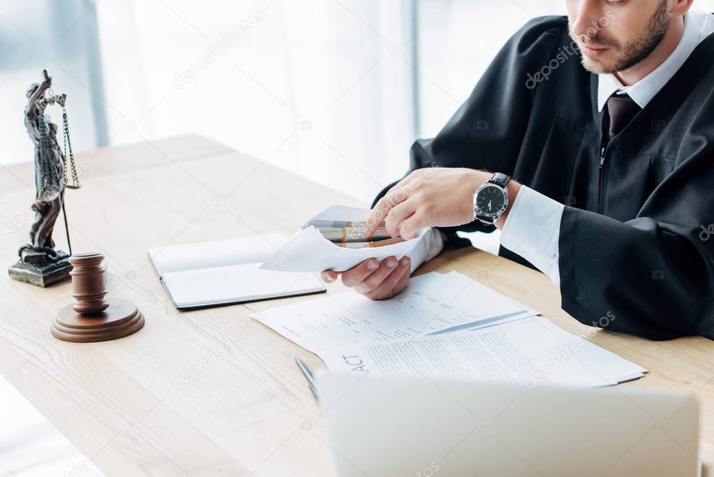 selective focus of wooden gavel near judge holding envelope with money 
