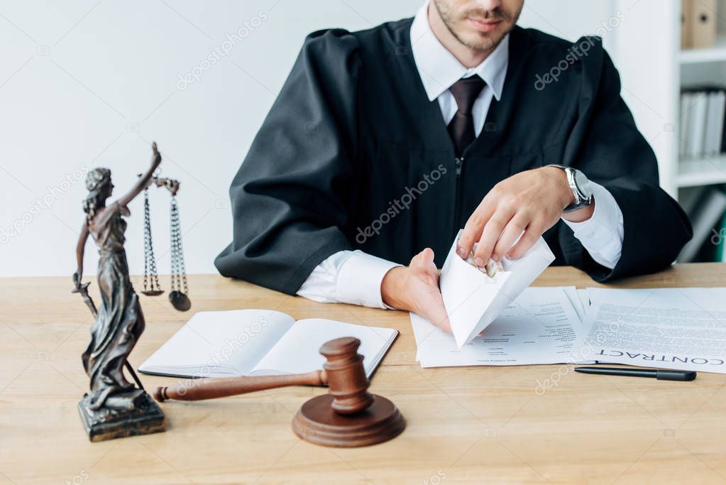 selective focus of judge holding envelope near gavel and statuette of justice 