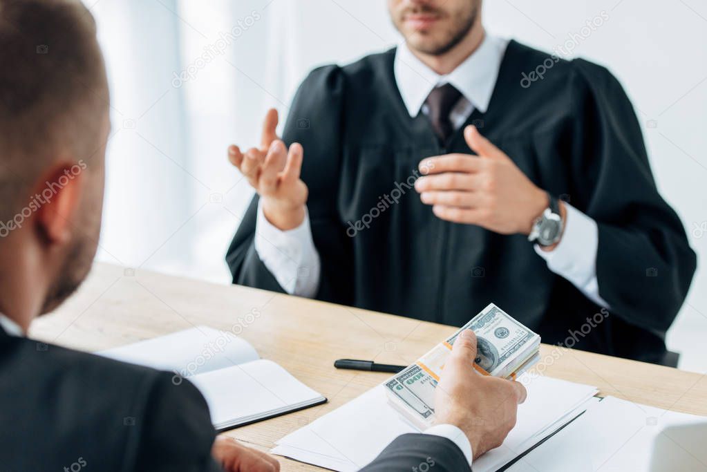selective focus of man giving money to judge sitting and gesturing near table 