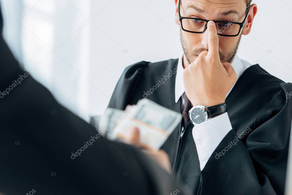 selective focus of judge touching glasses and looking at money hand of man 