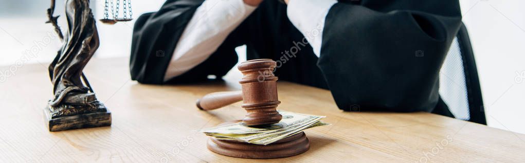 panoramic shot of judge near wooden gavel with money on table 