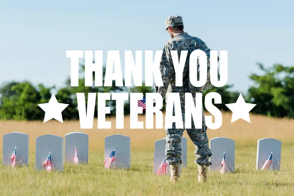 背面看军人拿着美国国旗附近的墓碑在墓地与感谢老兵插图 — 图库照片