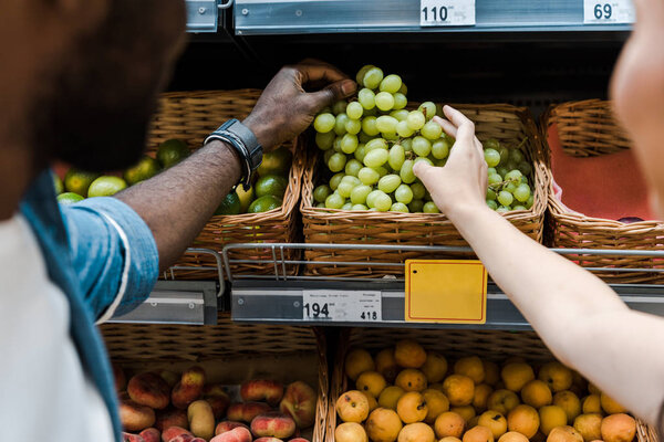 selective focus of african american man and woman taking grapes in store 