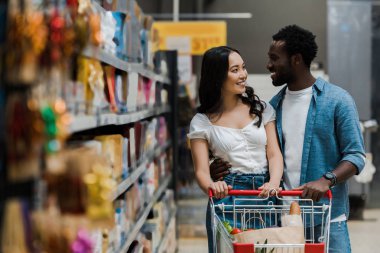 süpermarkette neşeli afrikalı-amerikalı erkek arkadaşı bakarak mutlu asyalı kadın seçici odak 