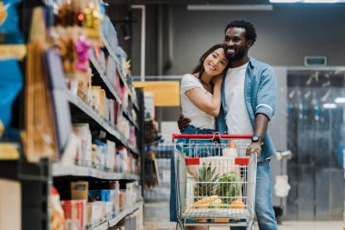 süpermarkette Asyalı kız arkadaşı sarılma neşeli afrikalı amerikalı adam seçici odak 