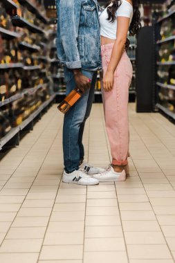 cropped view of african american man holding bottle with wine near woman in supermarket  clipart