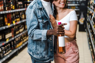 cropped view of african american man pointing with finger while holding bottle near cheerful girl  clipart