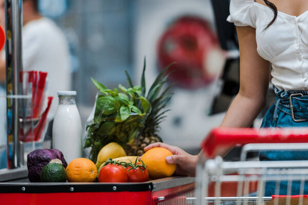 cropped view of woman holding orange near supermarket counter 