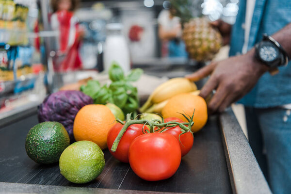 cropped view of african american man near supermarket counter with fruits and vegetables