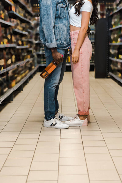 cropped view of african american man holding bottle with wine near woman in supermarket 
