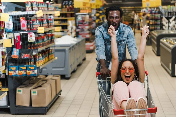 Excited African American Man Asian Girl Sunglasses Sitting Shopping Cart — Stock Photo, Image