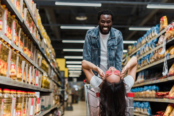 Boldog Afro Amerikai Férfi Nézi Stílusos Vidám Ázsiai Napszemüveg Bevásárlókocsi — Stock Fotó