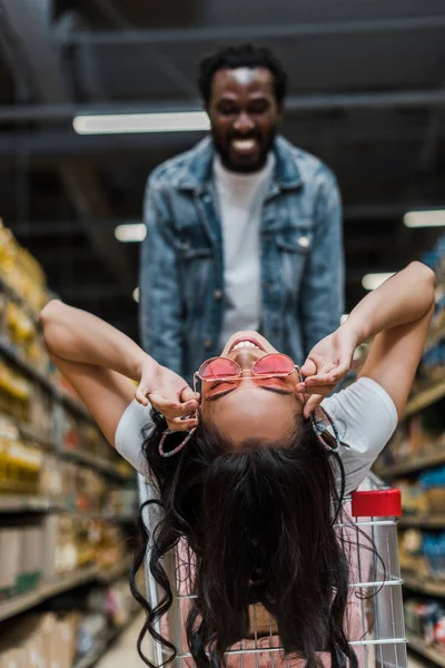 Selective Focus Cheerful Asian Woman Touching Sunglasses Sitting Shopping Cart — Stock Photo, Image