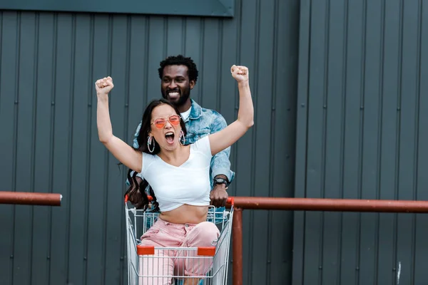 Mutlu Asyalı Kız Gesturing Sırasında Alışveriş Arabası Afrikalı Amerikalı Adam — Stok fotoğraf