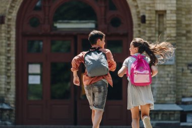 back view of two schoolkids with backpacks running in schoolyard clipart