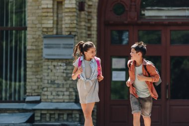 neşeli okul ve kız öğrenci gülümseyerek ve okul bahçesinde çalışırken birbirlerine bakıyor