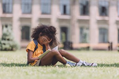 çim ve kitap okurken el ile yüz kapsayan yorgun afro-amerikan kız öğrenci