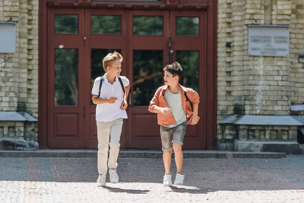 两个开朗的小学生在校园里奔跑 看着对方 — 图库照片