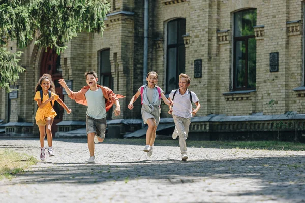 校庭で走りながら微笑む4人の愛らしい多文化の小学生 — ストック写真