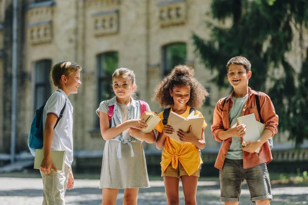Four Adorable Multicultural Schoolchildren Standing Schoolyard Holding Books — Stock Photo, Image