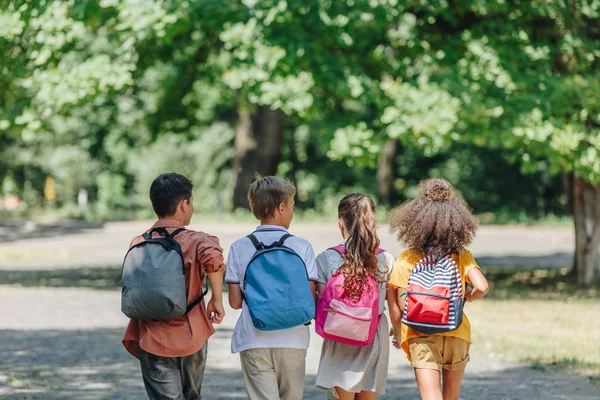 Vista Trasera Cuatro Amigos Multiculturales Con Mochilas Corriendo Parque Verano — Foto de Stock