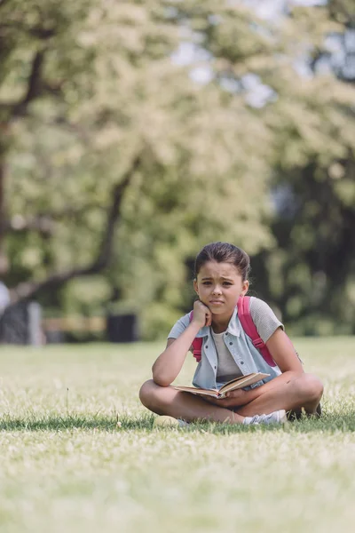 Cute Bored Schoolgirl Holding Book While Sitting Lawn Park — Stock Photo, Image