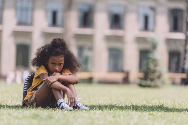 Upset African American Schoolgirl Looking Camera While Sitting Lawn — Stock Photo, Image