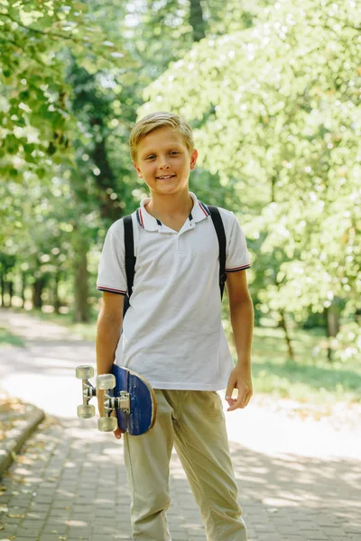 かわいい 陽気な男子生徒は スケートボードを持って 公園のカメラで笑顔 — ストック写真