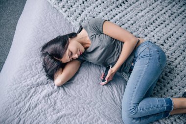 yatak odasında akıllı telefon ile yatakta üzgün depresif kadın üst görünümü
