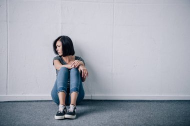 depressed lonely brunette woman sitting on floor at home clipart