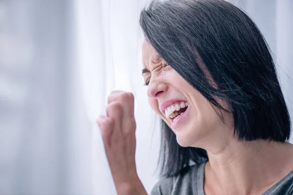 depressed brunette woman crying near window at home