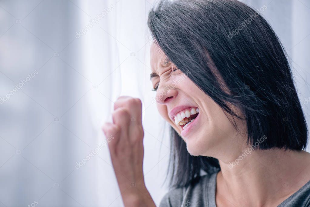 depressed brunette woman crying near window at home