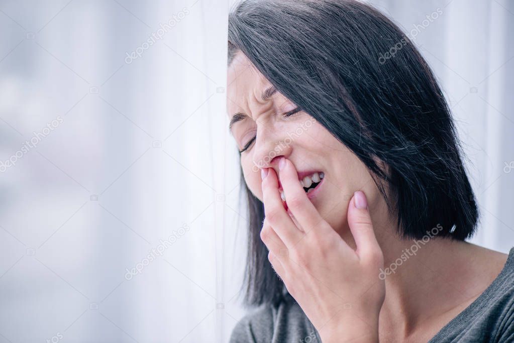 selective focus of depressed brunette woman covering mouth and crying at home