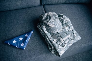military clothing and folded american flag on couch at home clipart