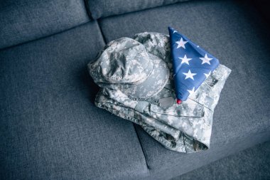 military clothing and folded american flag on couch at home clipart