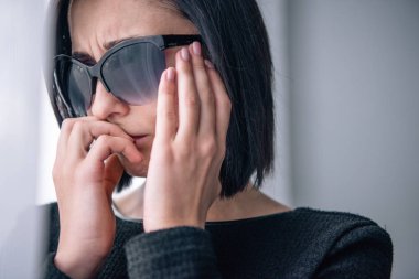depressed woman in sunglasses covering mouth and grieving at home clipart
