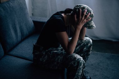depressed woman in military uniform with hands on head at home clipart