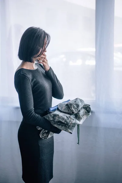 自宅で軍服を持つ落ち込んだ女性 — ストック写真