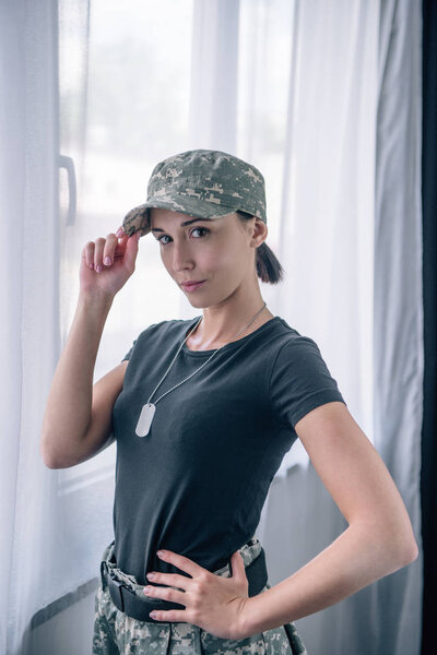 красивая женщина с рукой на бедре в военной форме смотрит в камеру дома
 
