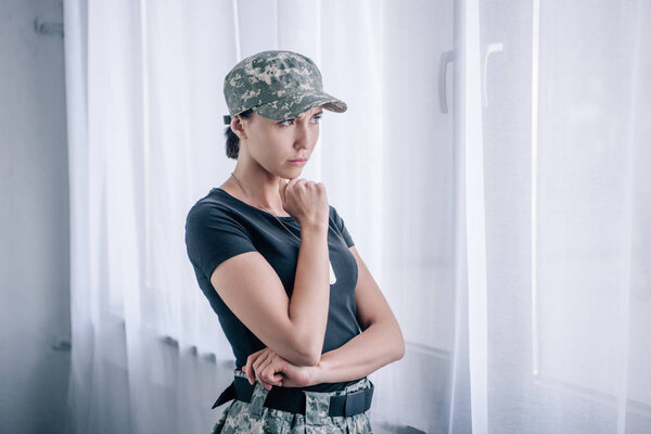 depressed pensive woman in military uniform touching chin at home
